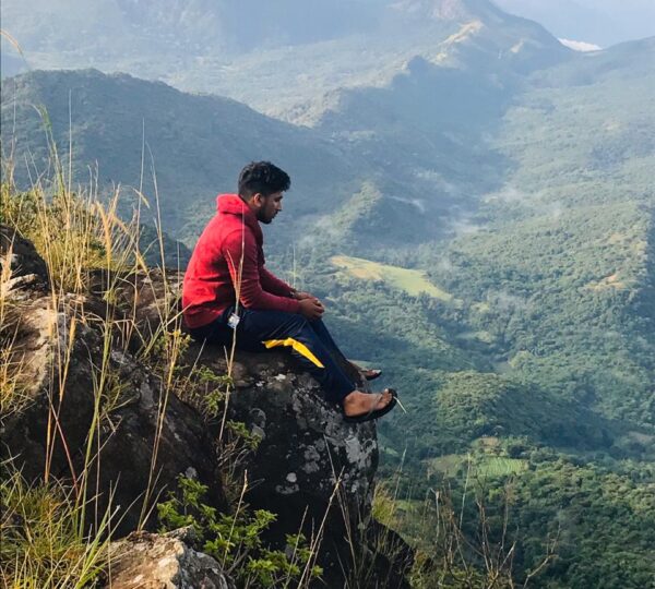 Hiker sitting on the cliff edge of Yahangala Bed Rock overlooking valley.